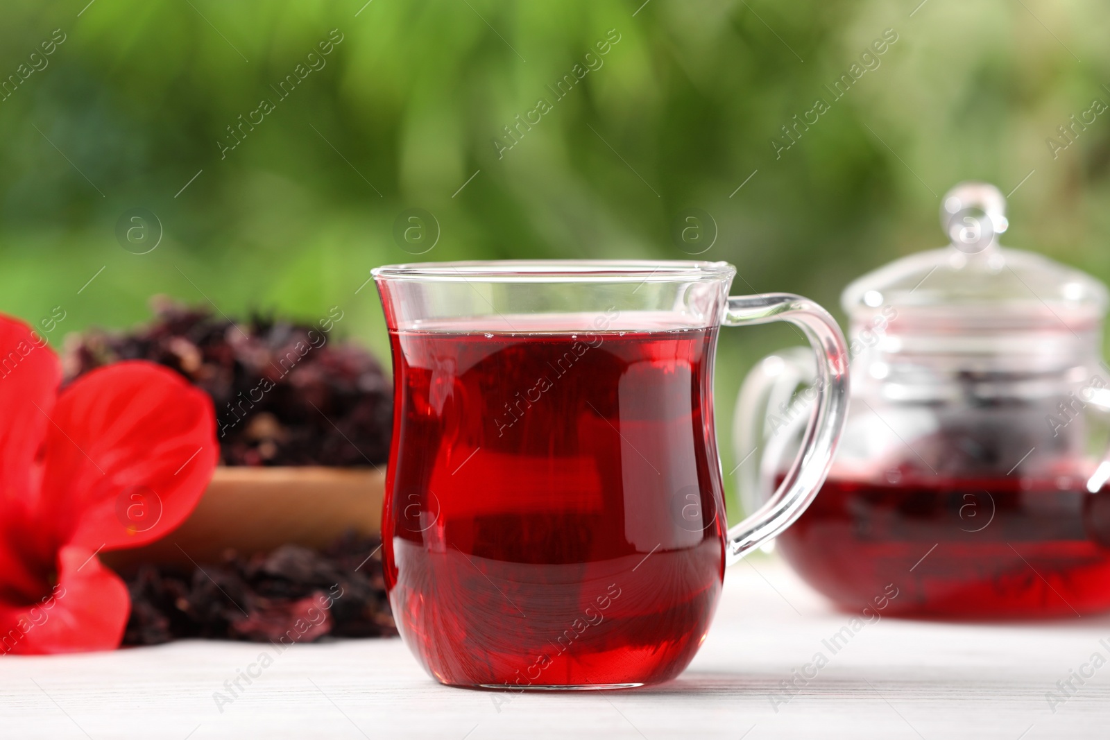 Photo of Glass cup of delicious hibiscus tea on white wooden table outdoors, closeup