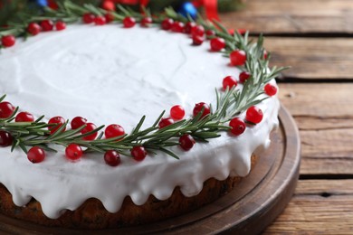 Traditional Christmas cake decorated with rosemary and cranberries on wooden table, closeup
