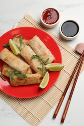 Photo of Tasty fried spring rolls, arugula, lime and sauces served on white table, flat lay