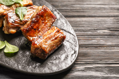 Photo of Delicious grilled ribs served on black wooden table, closeup. Space for text