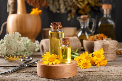 Photo of Bottles of essential oils, calendula flower and scissors on wooden table. Medicinal herbs