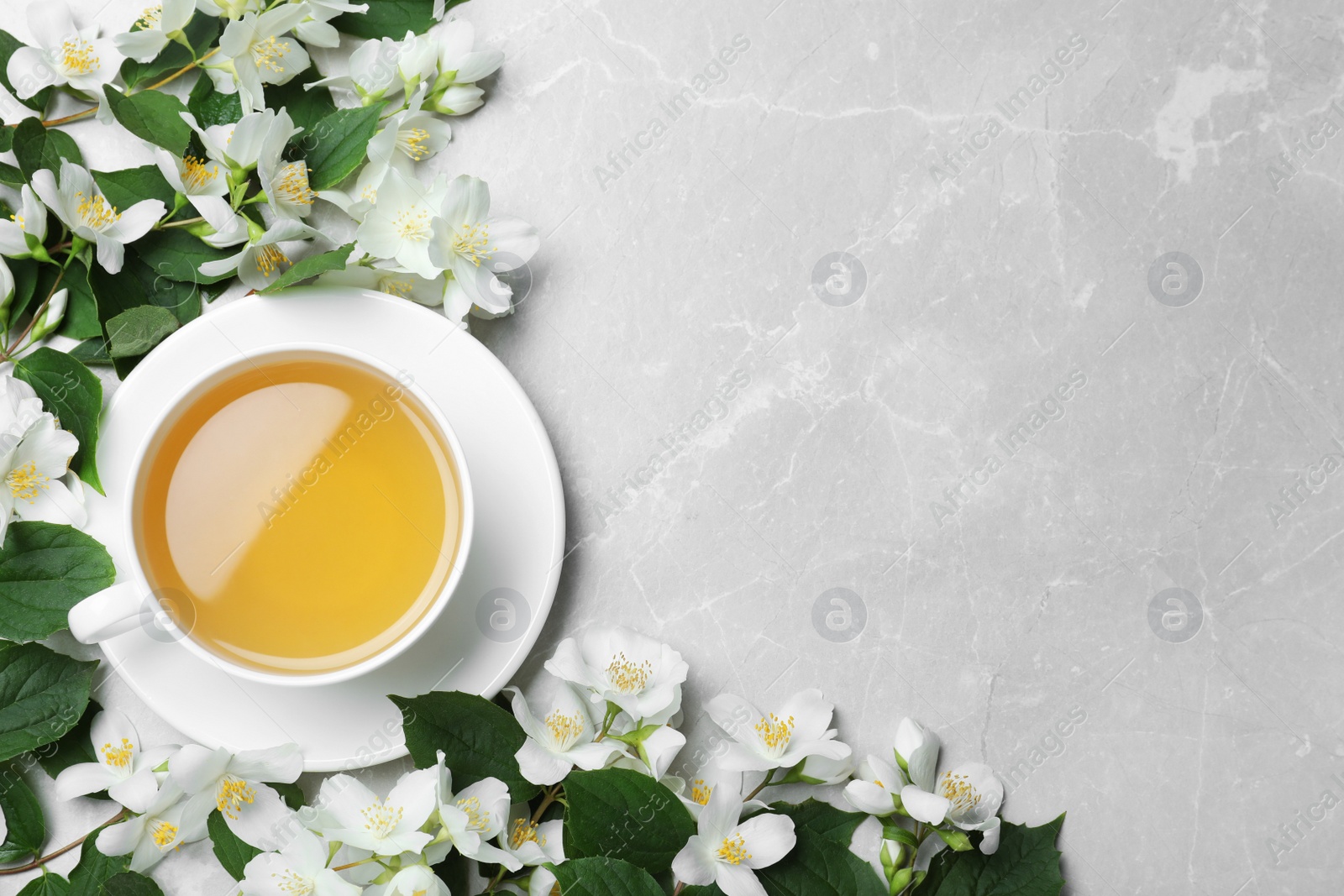 Photo of Cup of tea and fresh jasmine flowers on light grey marble table, flat lay. Space for text