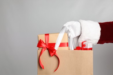 Photo of Santa holding paper bag with gift boxes on light grey background, closeup
