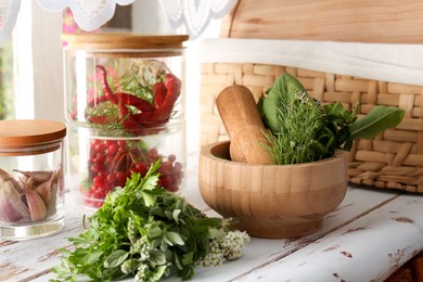 Photo of Mortar with pestle and fresh green herbs on white wooden table near window