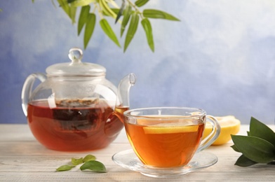 Photo of Glass cup and teapot with black tea on wooden table