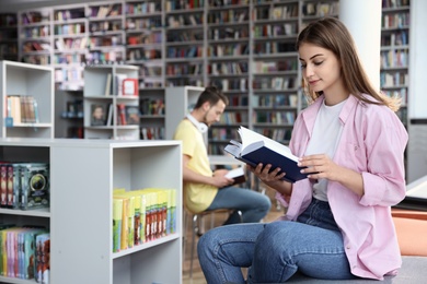 Young beautiful woman with book in library