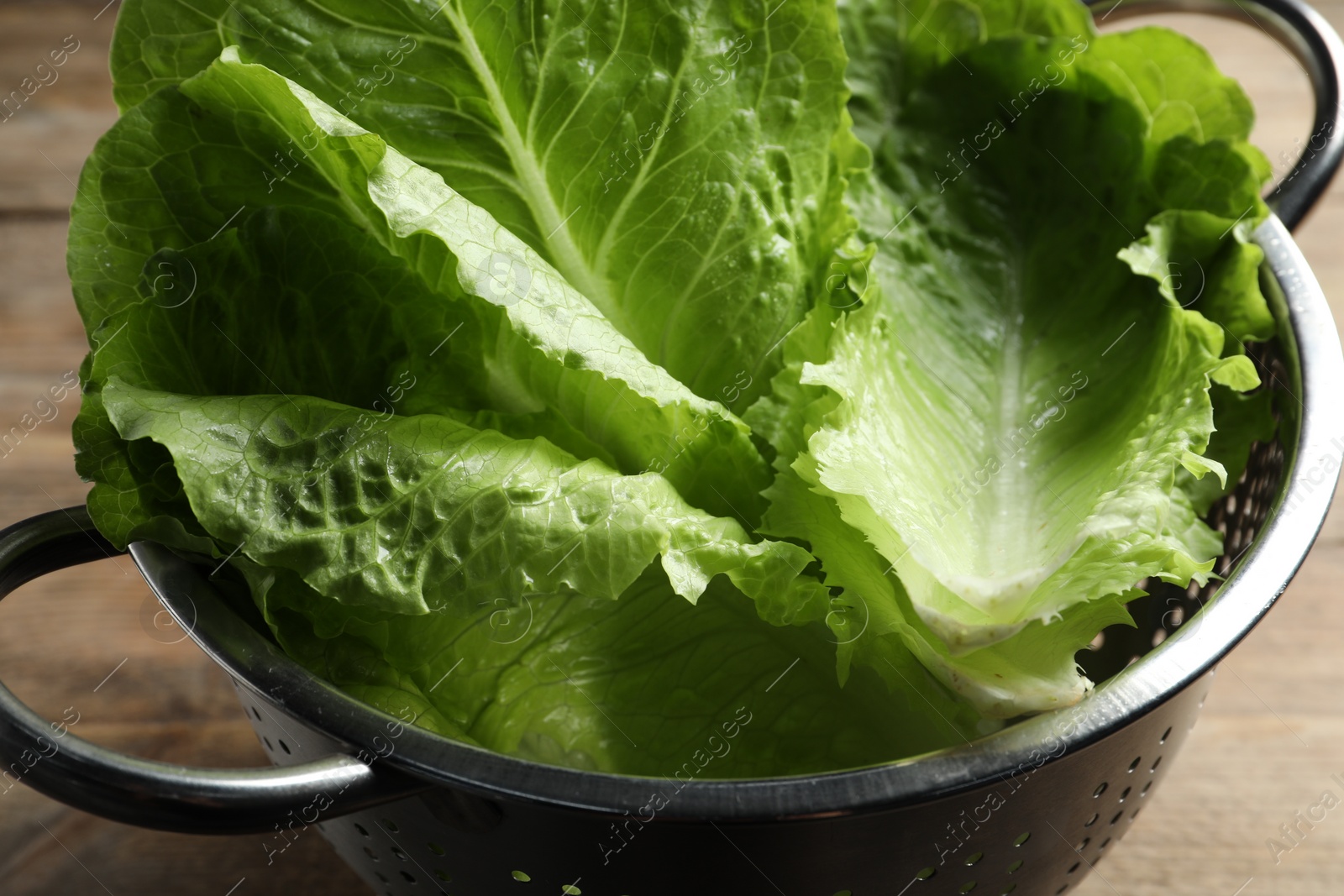 Photo of Colander with fresh leaves of green romaine lettuce on table, closeup