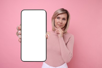 Thoughtful woman showing mobile phone with blank screen on pink background. Mockup for design