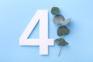 Paper number 4 and eucalyptus branch on light blue background, top view