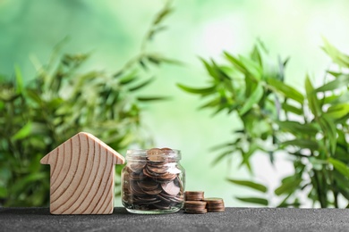 House model and jar with coins on table against blurred background. Space for text