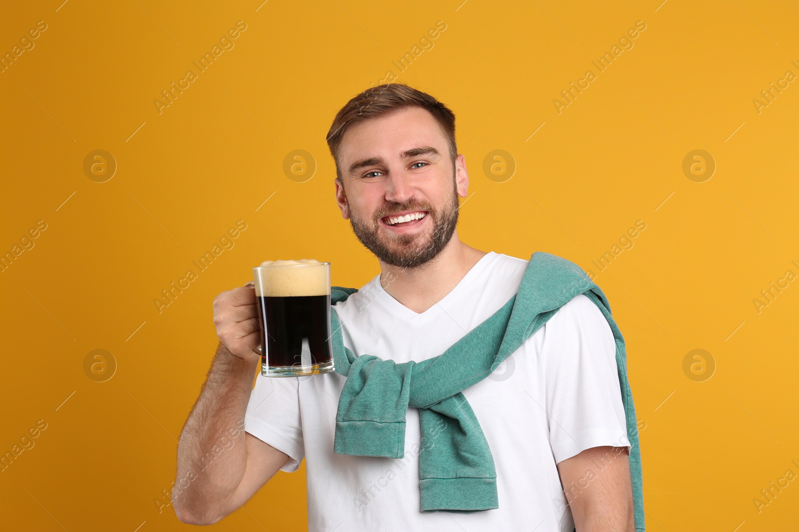 Photo of Handsome man with cold kvass on yellow background. Traditional Russian summer drink