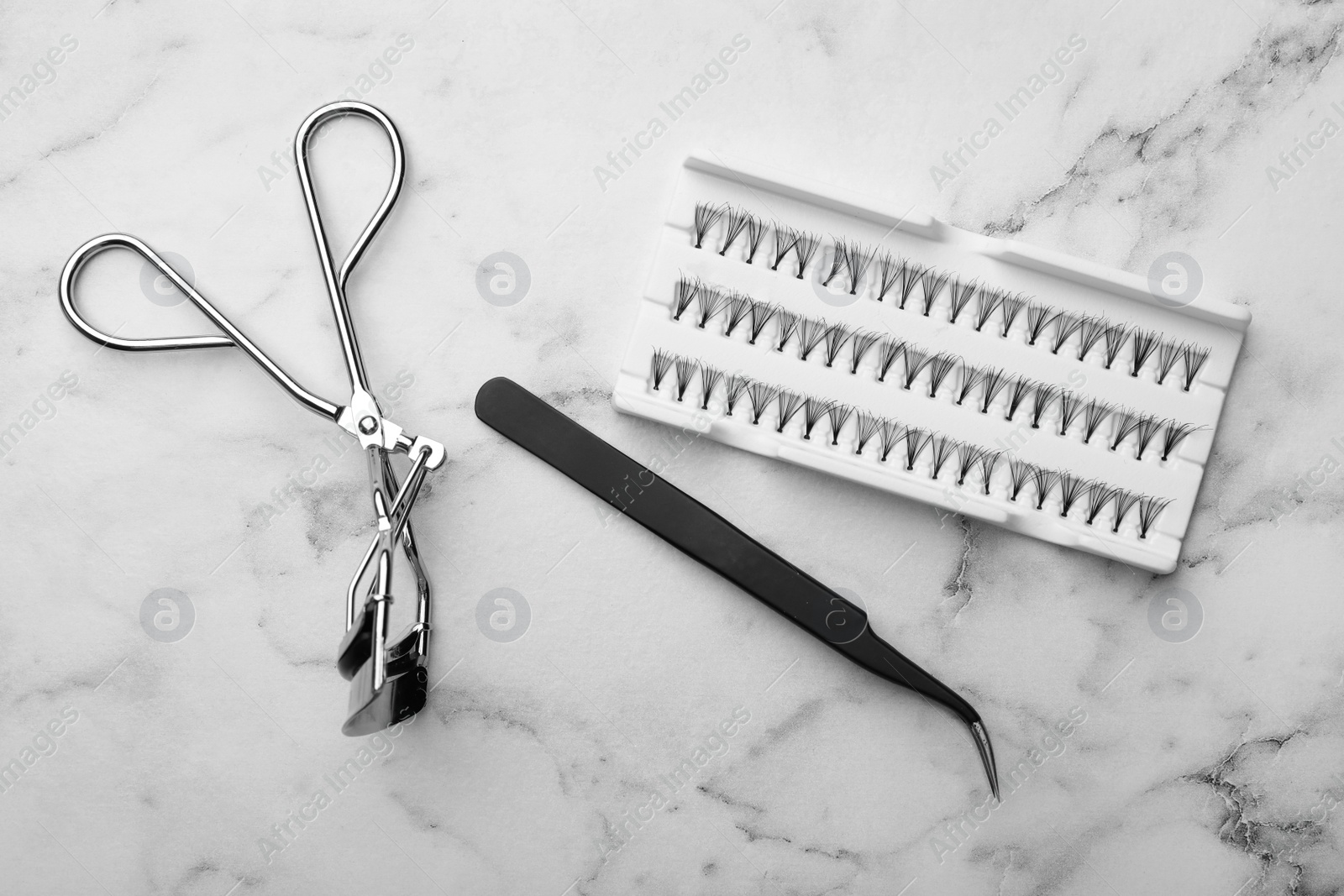 Photo of Artificial eyelashes and accessories on marble background, flat lay