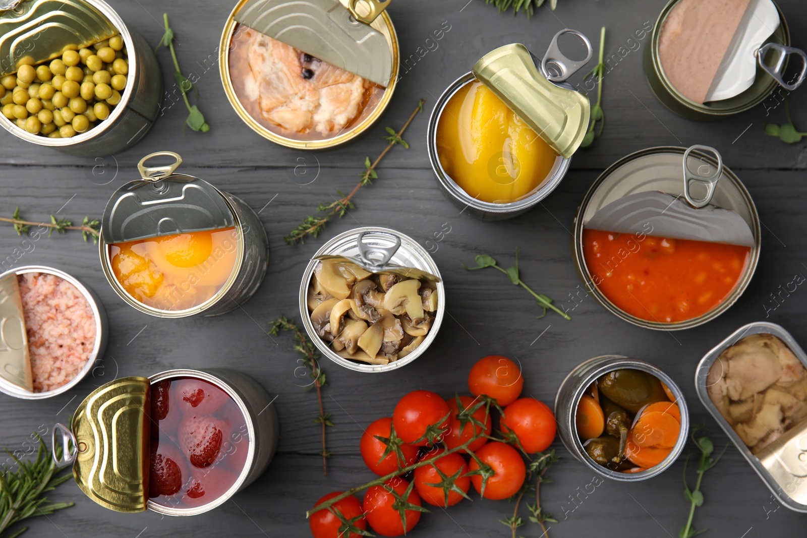 Photo of Open tin cans with different products on gray wooden table, flat lay