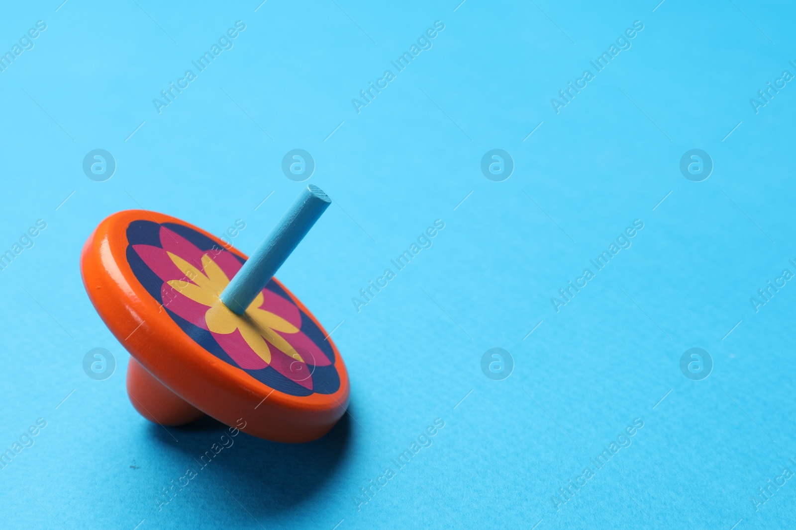 Photo of One colorful spinning top on light blue background, space for text