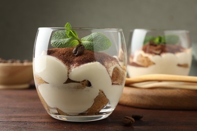 Delicious tiramisu in glasses, mint leaves and coffee beans on wooden table, closeup