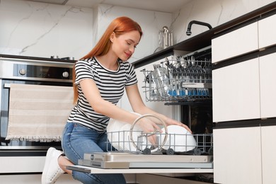 Photo of Woman loading dishwasher with plates in kitchen