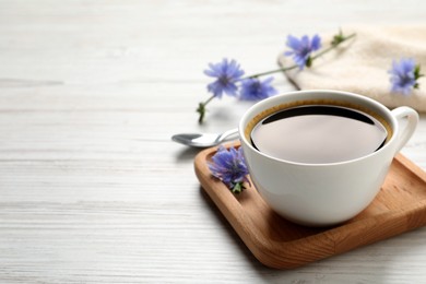 Photo of Cup of delicious chicory drink and flowers on white wooden table. Space for text