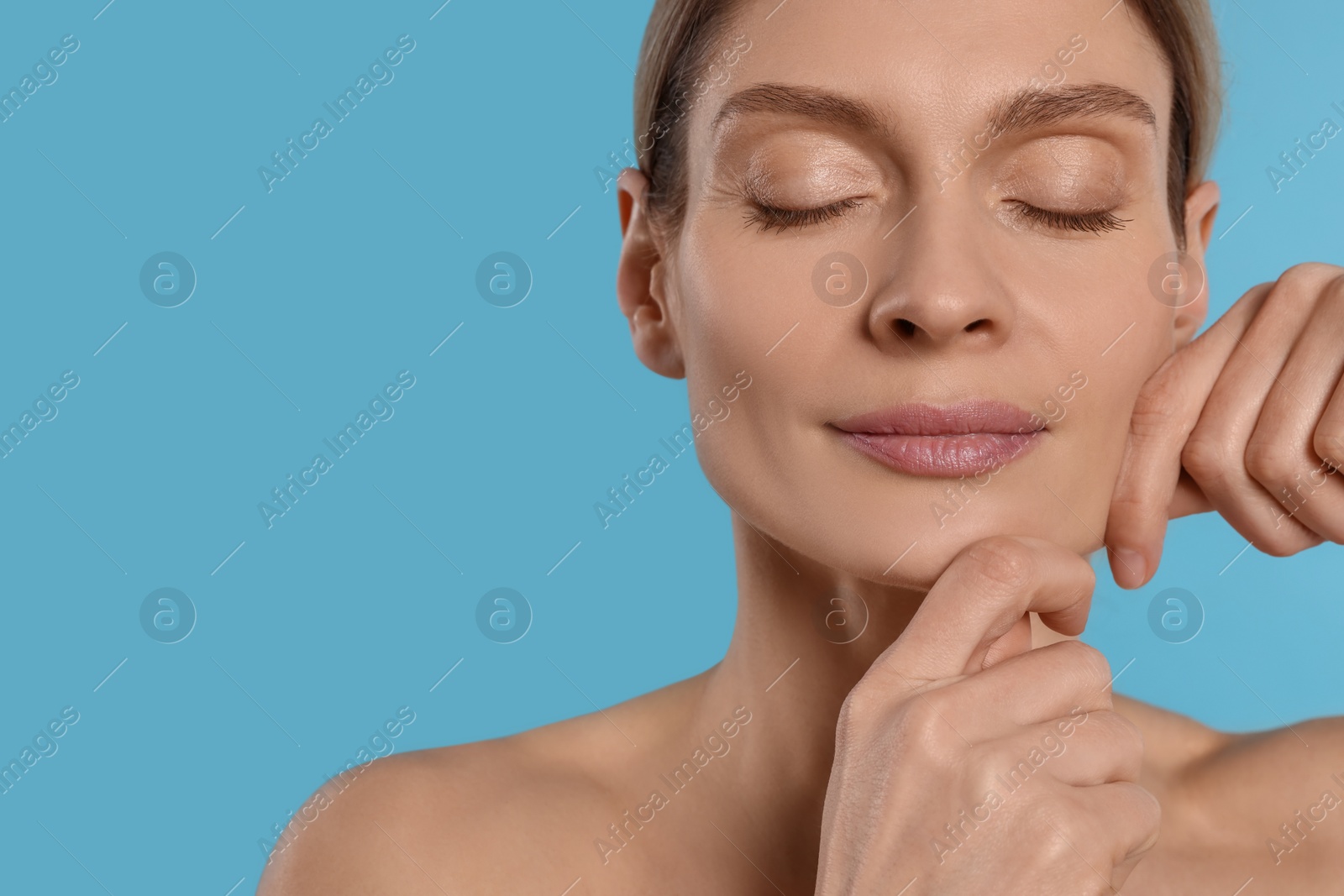 Photo of Woman massaging her face on turquoise background. Space for text