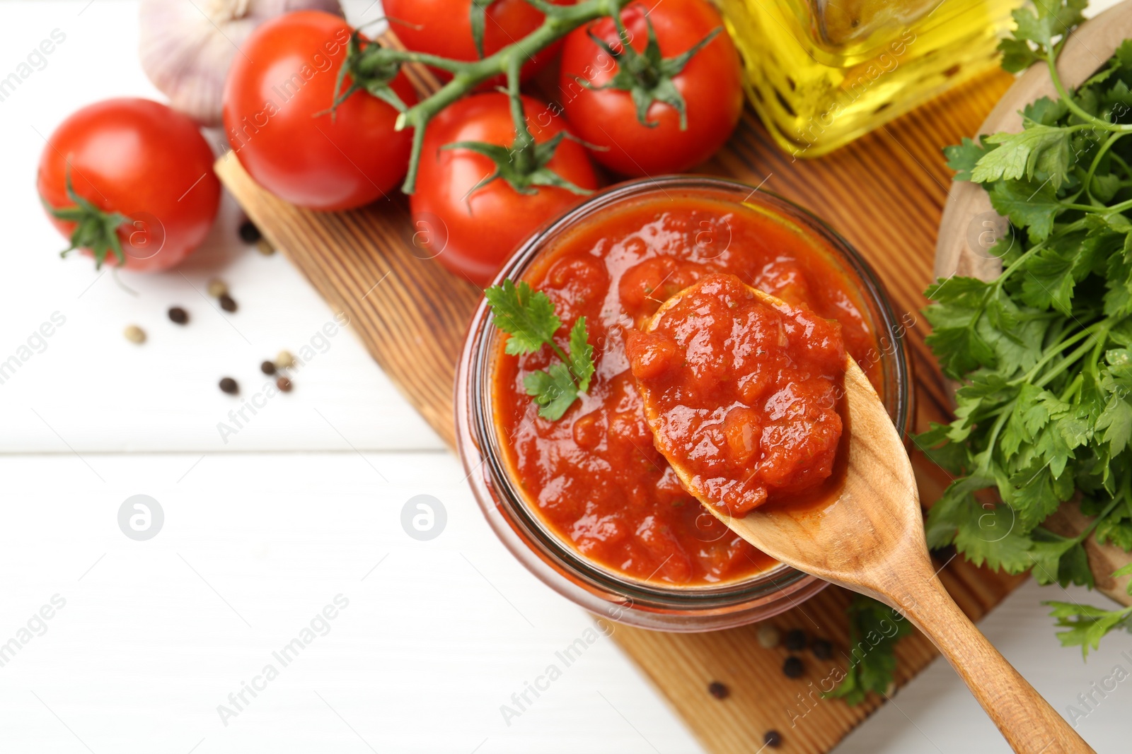 Photo of Homemade tomato sauce in jar, spoon and fresh ingredients on white wooden table, flat lay