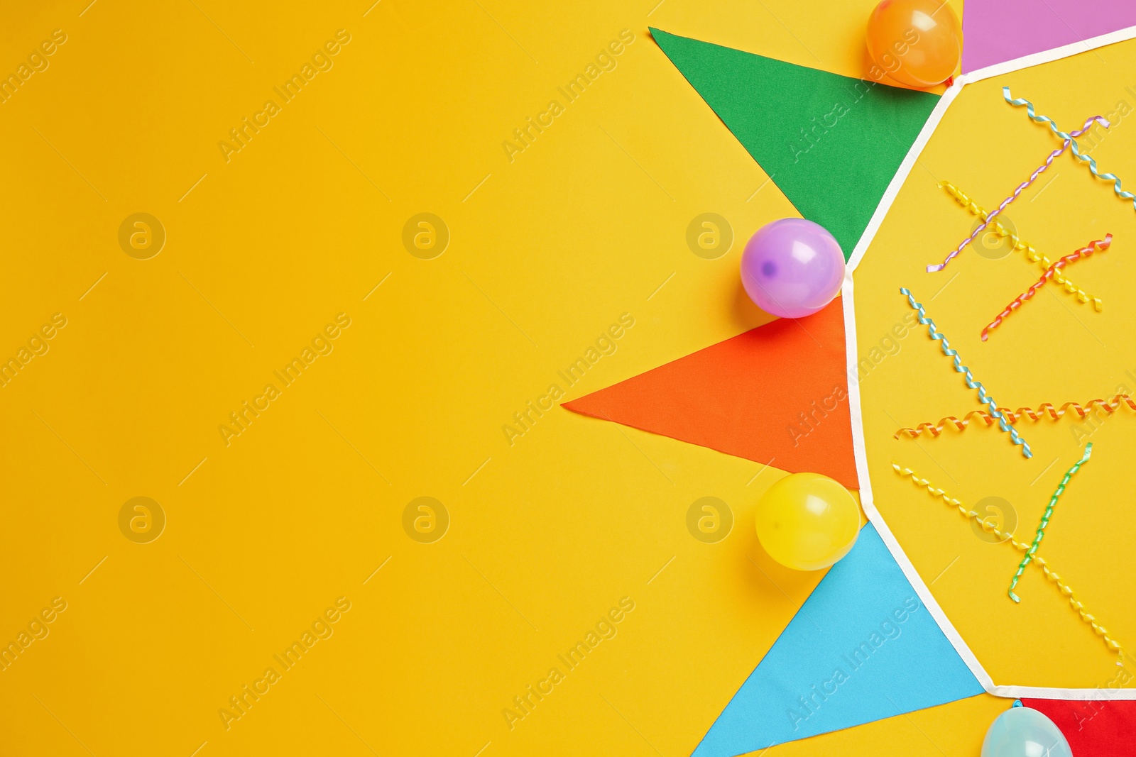 Photo of Bunting with colorful triangular flags and other festive decor on yellow background, flat lay. Space for text