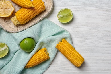 Flat lay composition with corn cobs and citrus fruits on white wooden background. Space for text