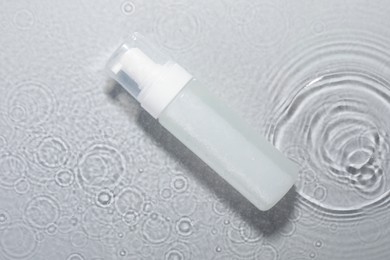 Photo of Bottle of facial cleanser in water against light grey background, top view