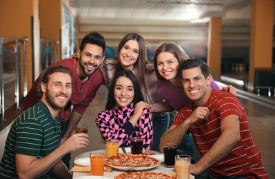 Group of friends with drinks and pizza in bowling club