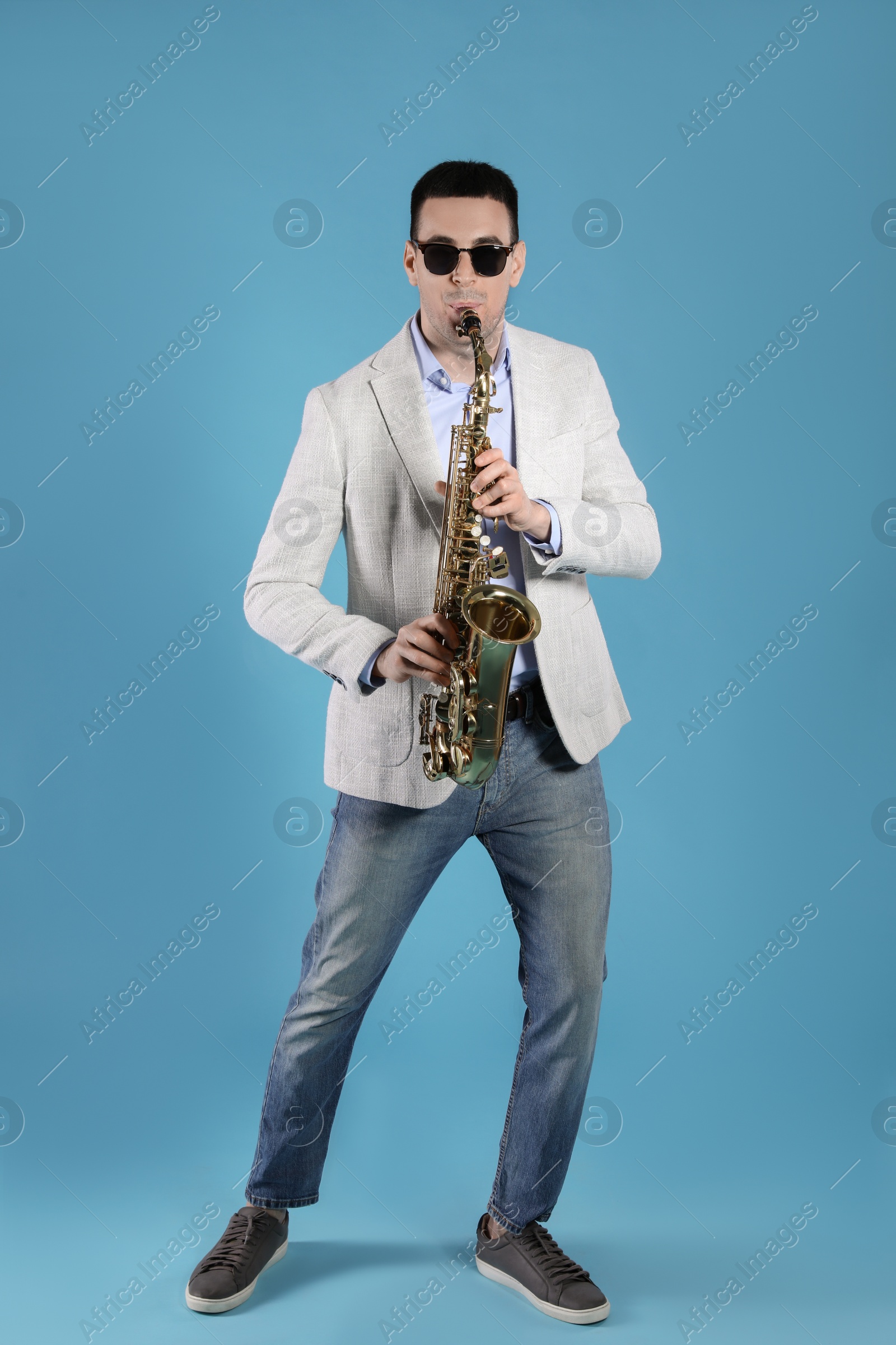 Photo of Young man playing saxophone on light blue background