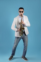 Young man playing saxophone on light blue background