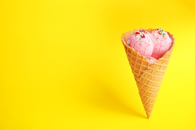 Photo of Delicious ice cream in wafer cone on yellow background. Space for text