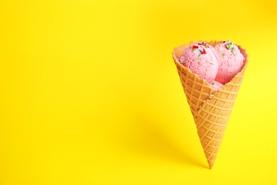 Delicious ice cream in wafer cone on yellow background. Space for text