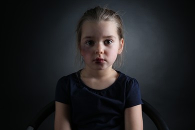 Photo of Little girl with bruises on face against dark background. Domestic violence victim