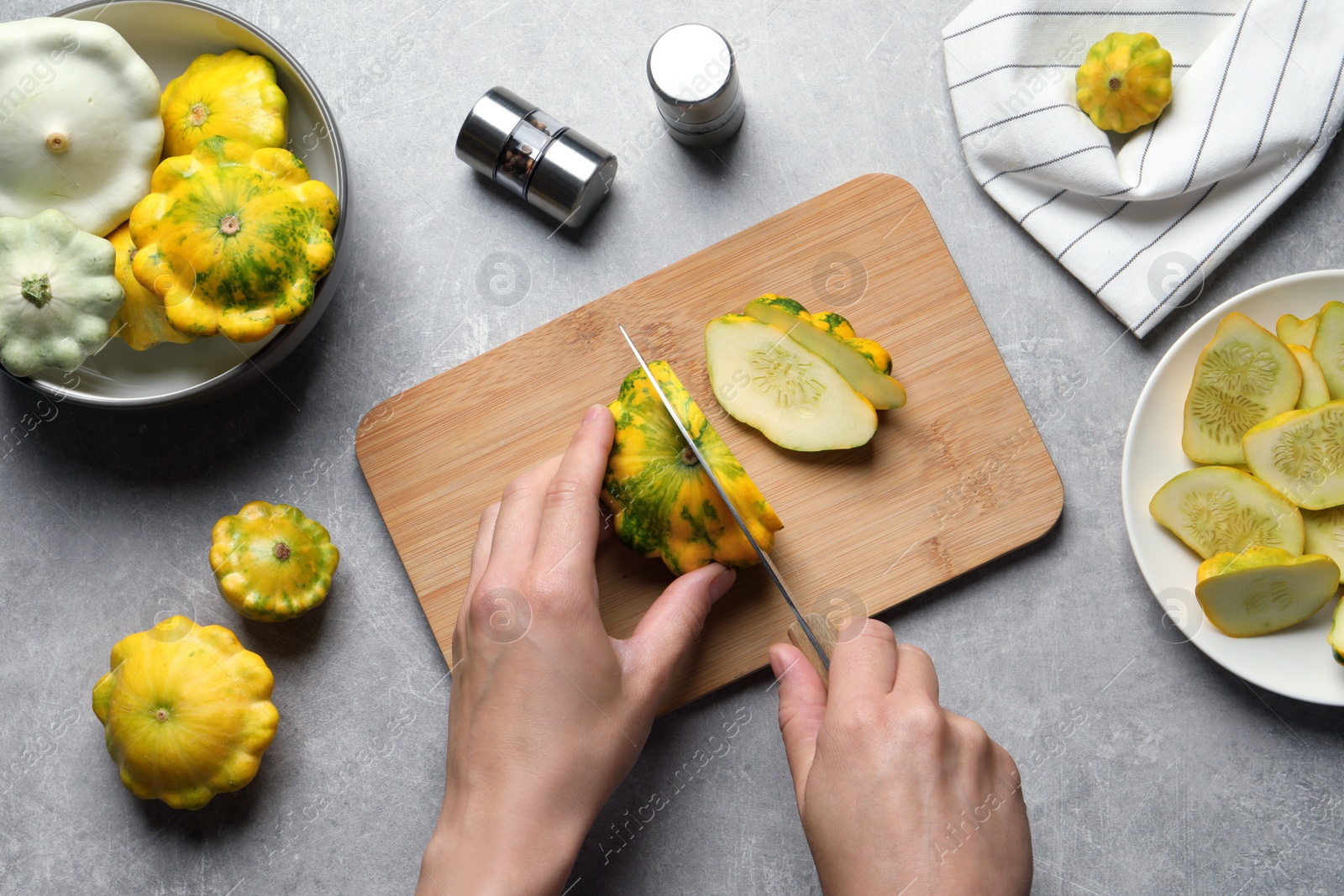 Photo of Woman cutting ripe yellow pattypan squash at grey table, top view