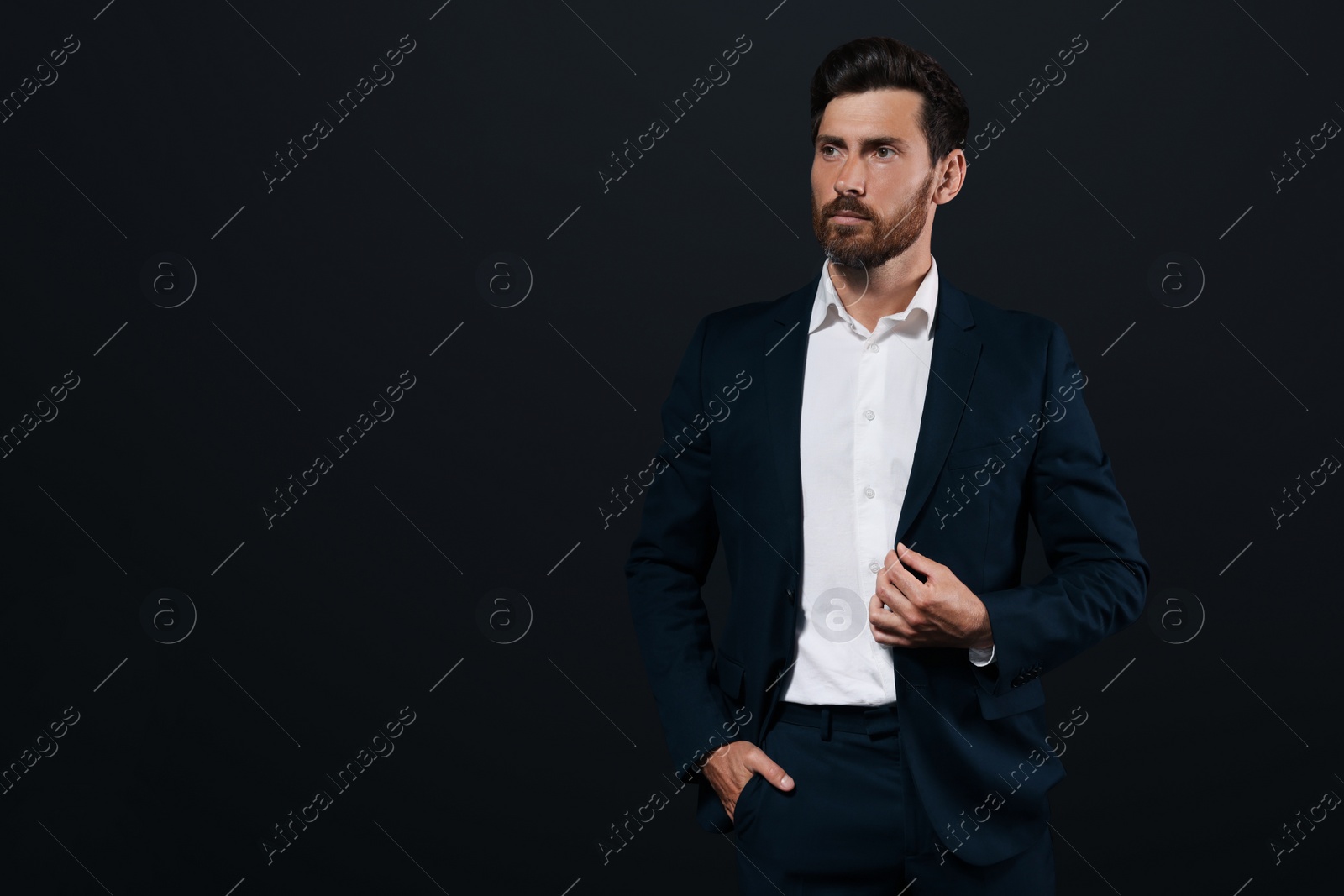 Photo of Portrait of handsome bearded man in suit looking away on black background. Space for text