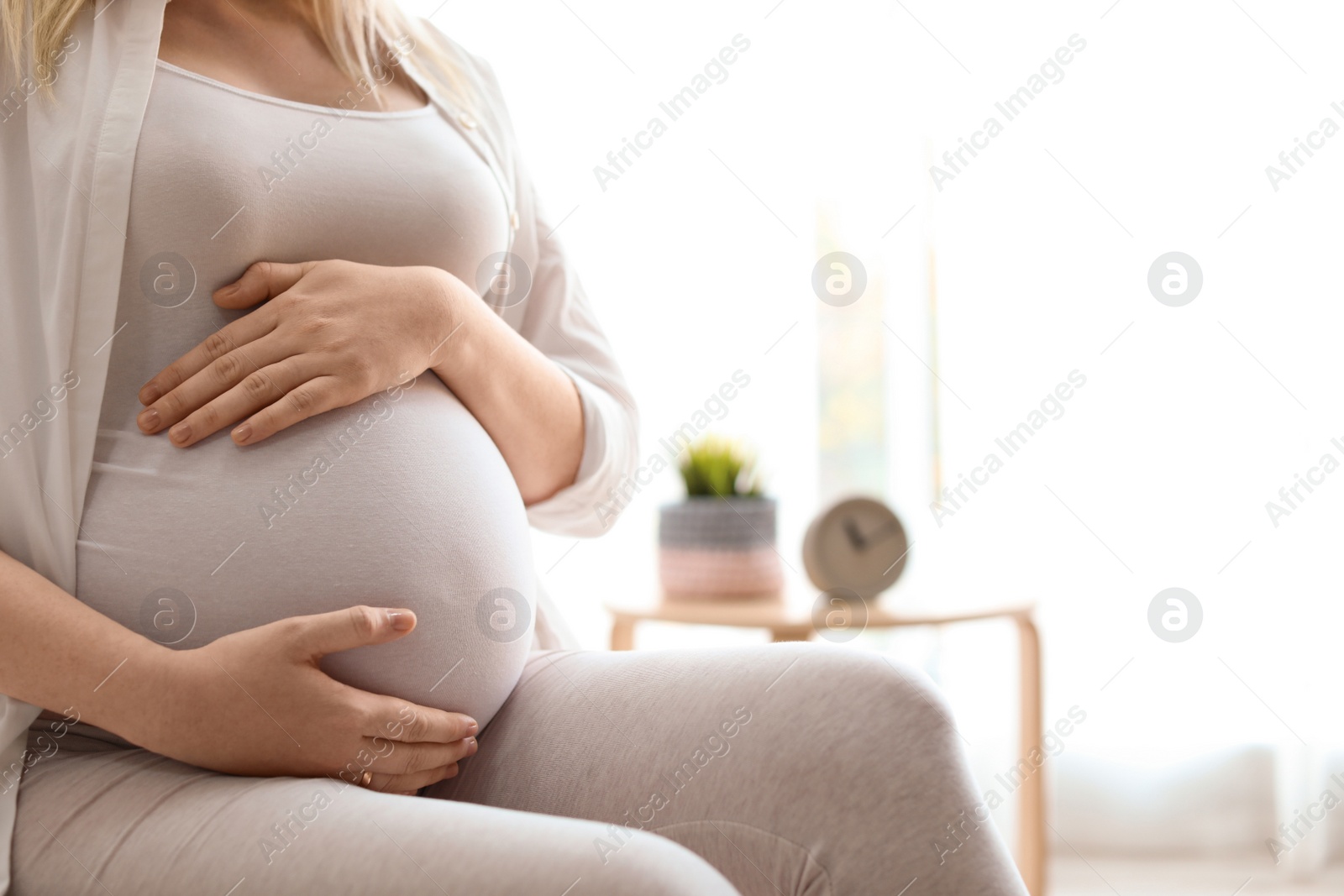 Photo of Pregnant woman sitting in light room at home, closeup