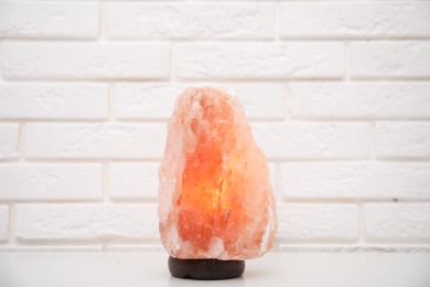 Photo of Himalayan salt lamp on table near white brick wall