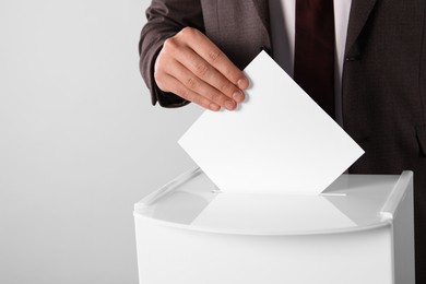 Man putting his vote into ballot box on light grey background, closeup. Space for text