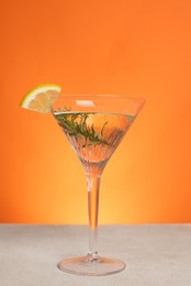 Photo of Martini glass of refreshing cocktail with lemon slice and rosemary on light grey table