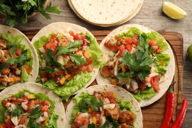 Delicious tacos with vegetables, meat and lime on wooden table, flat lay