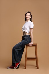 Photo of Smiling tattooed woman sitting on stool against beige background
