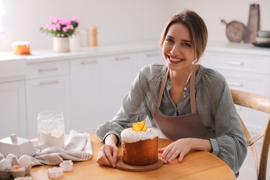 Photo of Young woman with traditional decorated Easter cake at wooden table in kitchen. Space for text