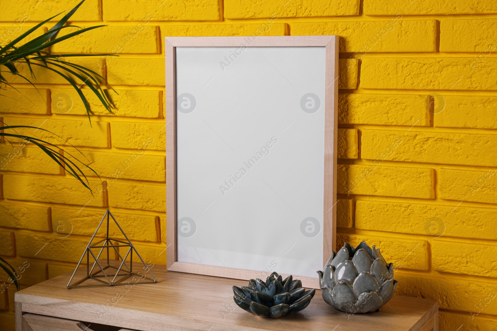 Photo of Empty frame and decor on wooden cabinet near yellow brick wall. Mockup for design