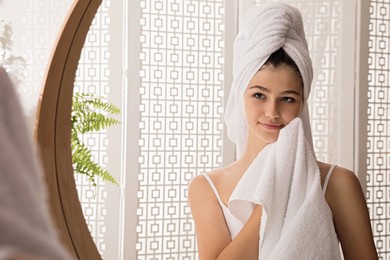 Photo of Beautiful teenage girl wiping face with towel near mirror at home