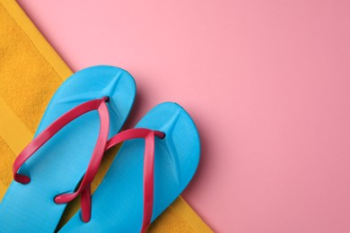 Photo of Light blue flip flops and yellow towel on pink background, top view with space for text. Beach accessories