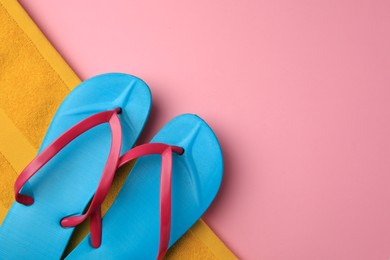 Light blue flip flops and yellow towel on pink background, top view with space for text. Beach accessories