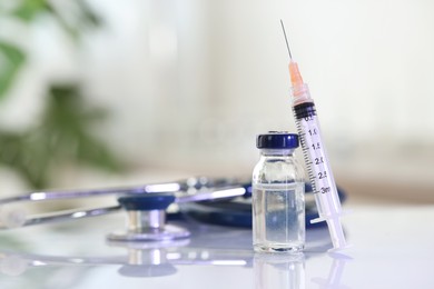 Photo of Glass vial, syringe and stethoscope on white table, closeup