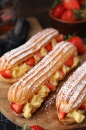 Photo of Delicious eclairs filled with cream and strawberries on table, closeup