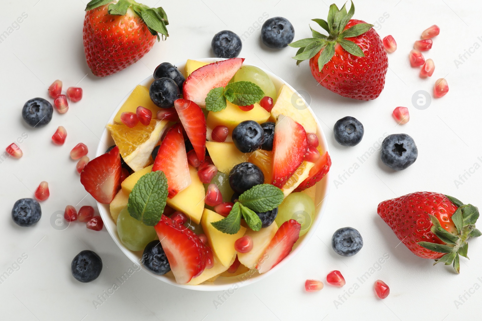 Photo of Tasty fruit salad in bowl and ingredients on white table, flat lay