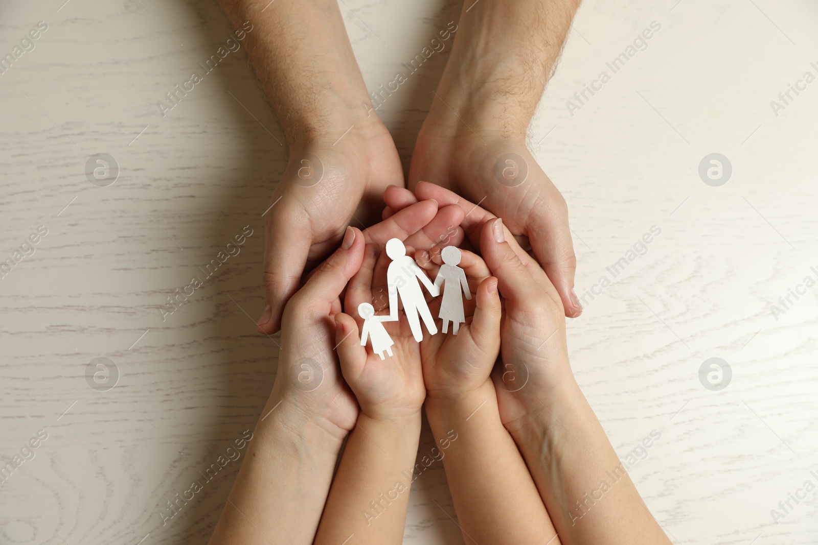 Photo of Parents and child holding paper cutout of family at white wooden table, top view