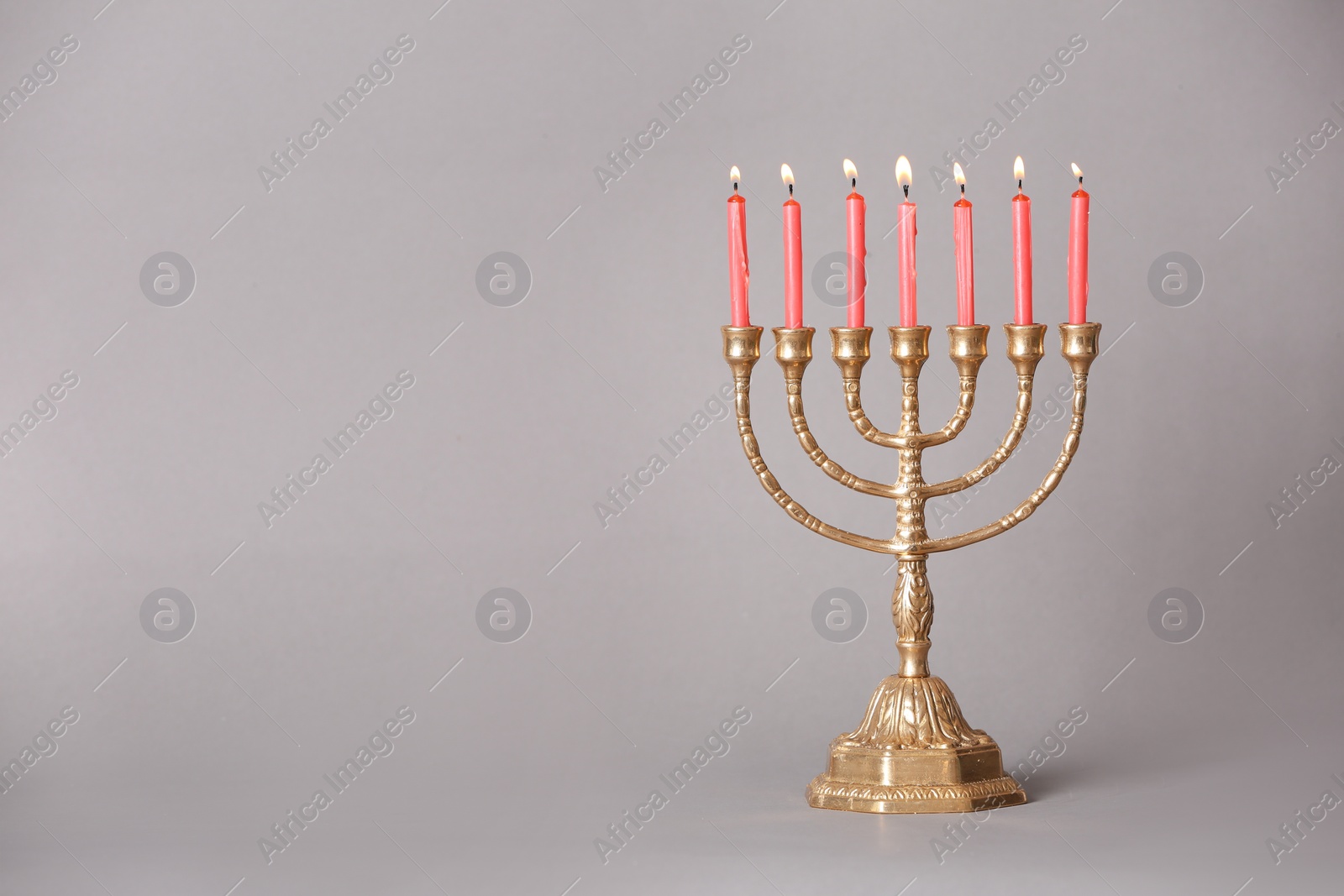 Photo of Golden menorah with burning candles on light grey background, space for text